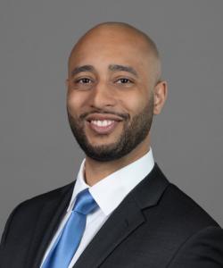 Dr. Alexander, physiatrist, smiling and wearing a black suit with a blue tie.